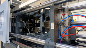 Industrial manufacturing machine with large metal rollers, blue/red hydraulic hoses, and control components.