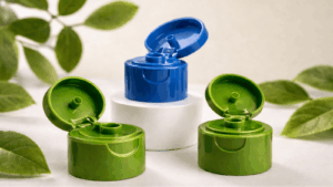 Three plastic bottle caps (two green, one blue) arranged on a white display, blue cap open while green caps are closed, with green leaves in the background.